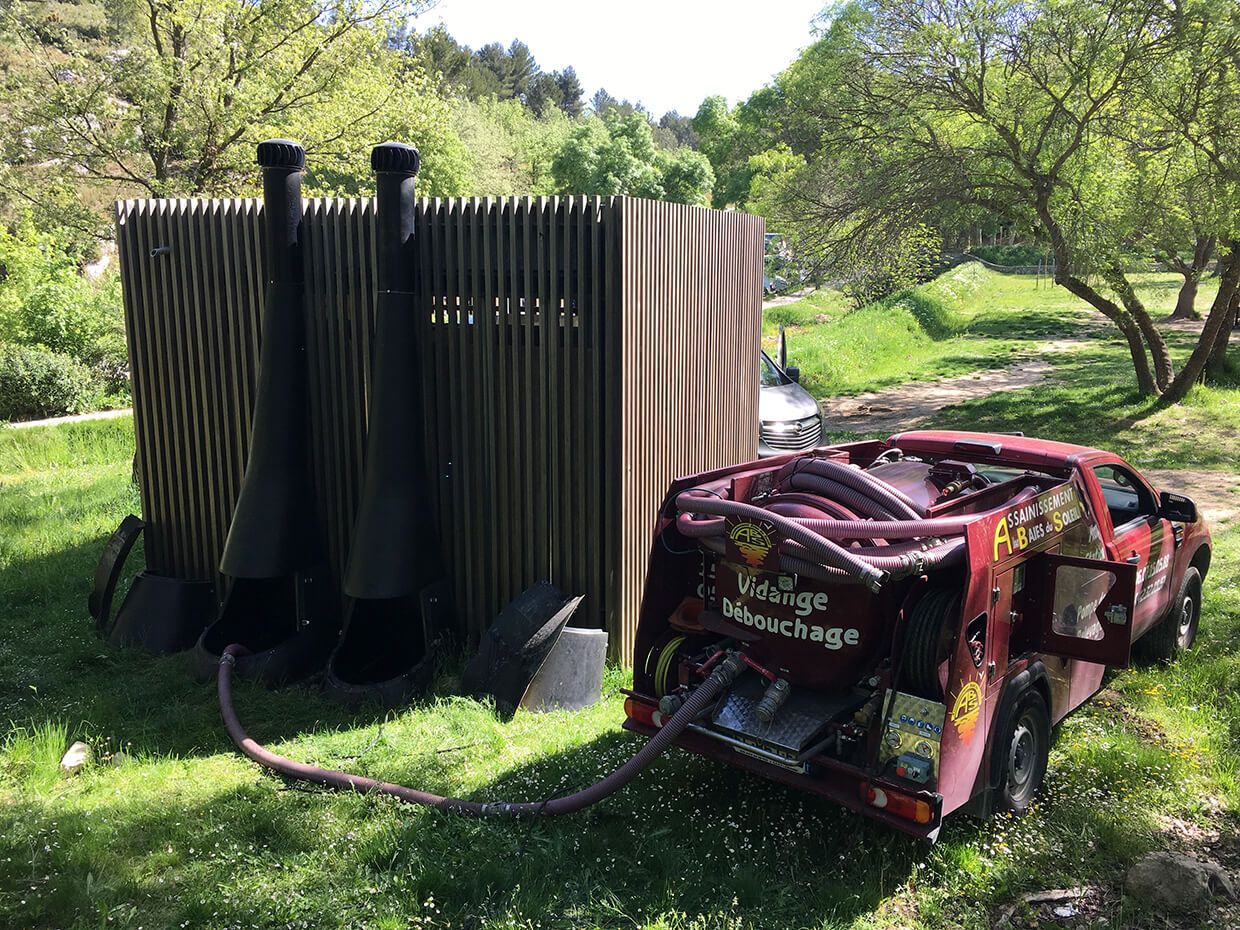 Véhicule rouge d'assainissement à côté d'une structure rayée dans une zone boisée et herbeuse