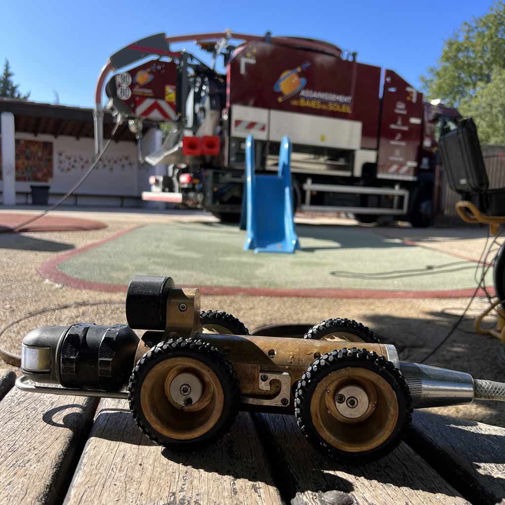 Camion d'assainissement sur le trottoir devant un camion utilitaire rouge et un cône bleu, à l'extérieur