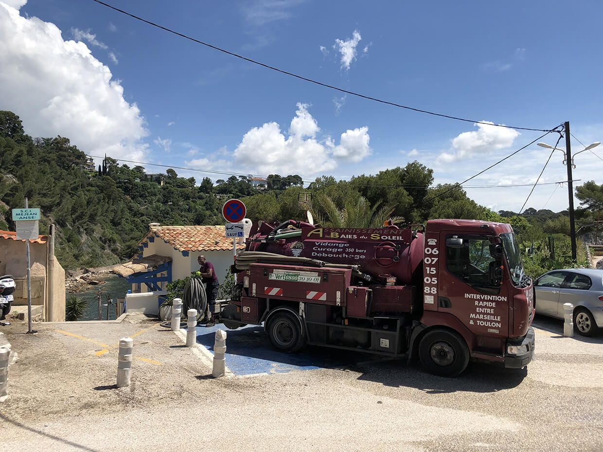 Un camion d'assainissement rouge est garée sur un chemin de terre près d'un chantier, sous un ciel bleu.