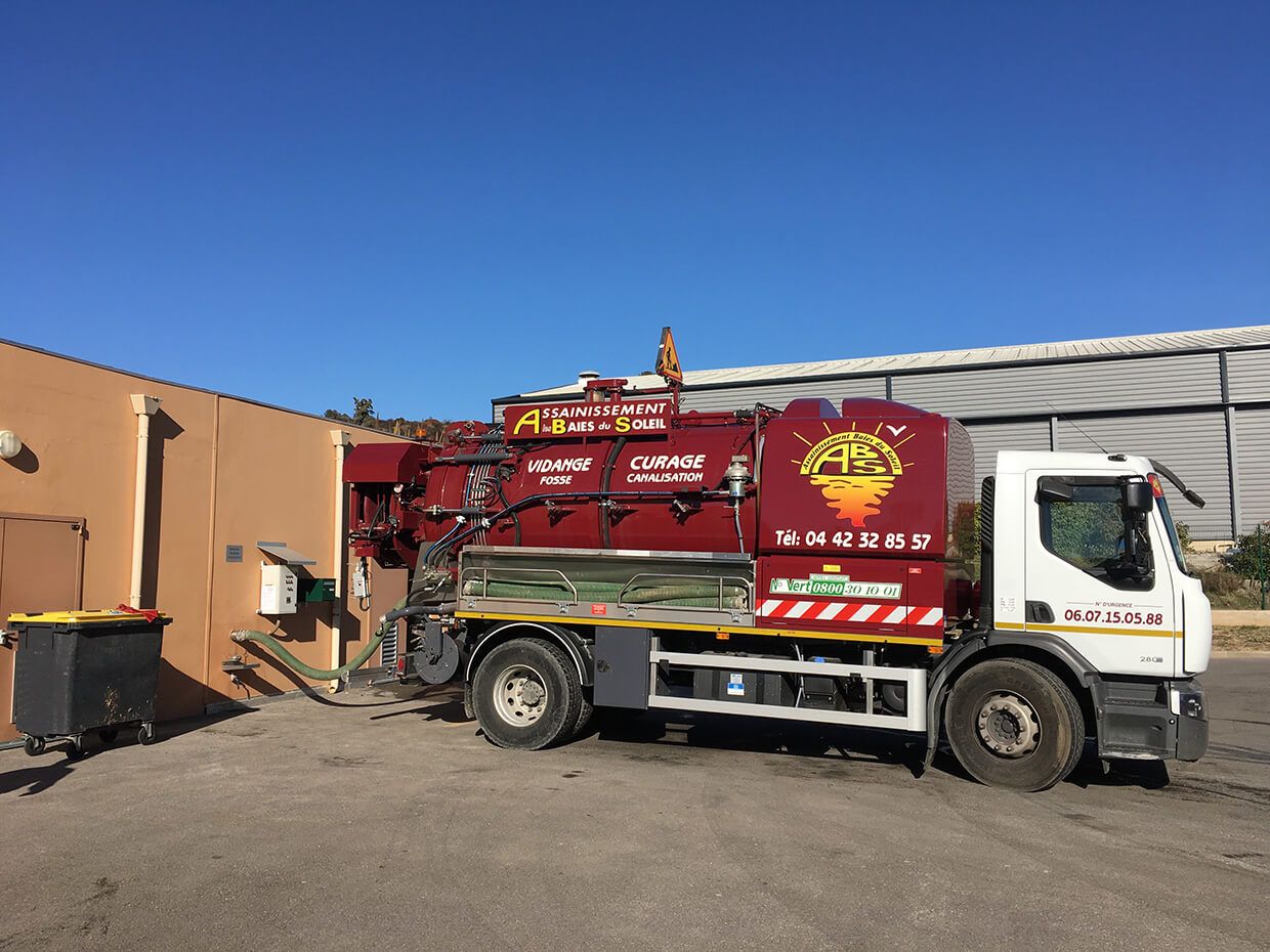 Camion d'assainissement rouge garé à côté d'un bâtiment sous un ciel d'un bleu éclatant