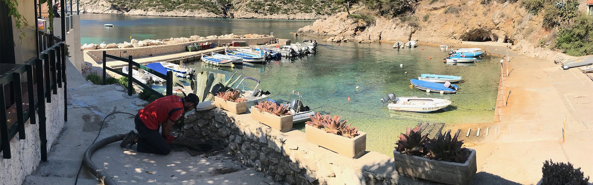Crique rocheuse avec des nageurs, des personnes prenant un bain de soleil et de petits bateaux dans une eau bleue et limpide.