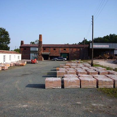 Cour industrielle extérieure avec des palettes empilées, des bâtiments en briques et des véhicules stationnés sous un ciel dégagé
