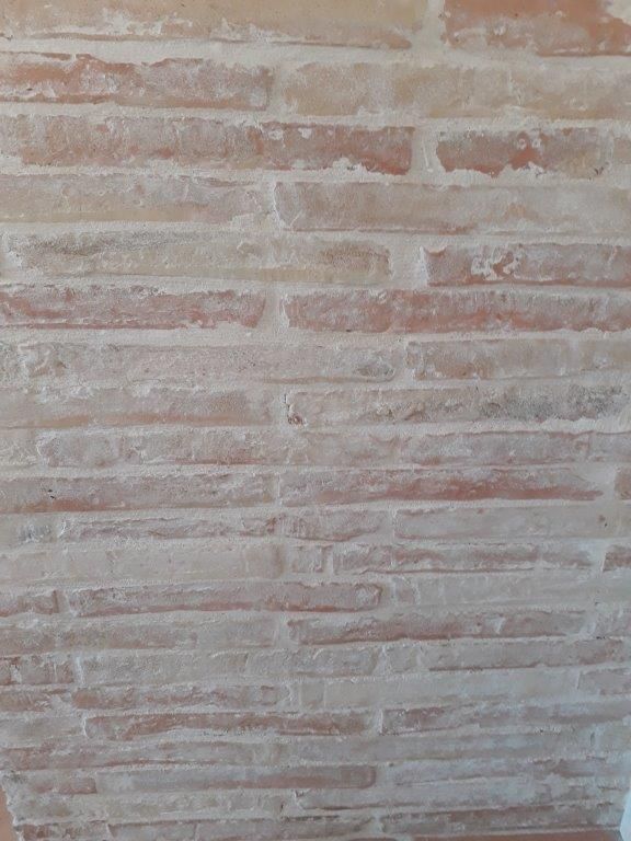 Mur en briques beige clair avec mortier blanc, légèrement patiné et texturé.