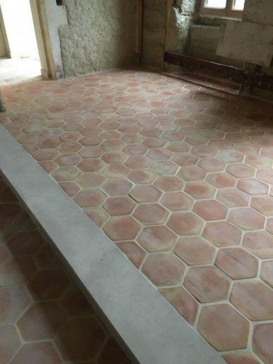 Pièce vide avec un sol en carrelage hexagonal rose et des fenêtres sur la droite.