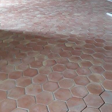 Pavés hexagonaux en briques rouges projetant une ombre diagonale sur une partie du sol.