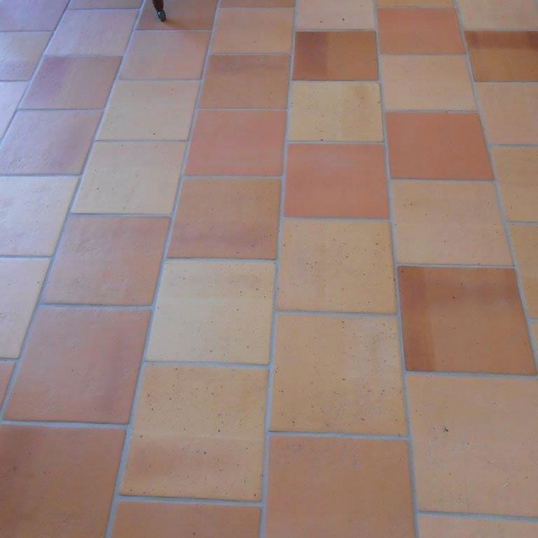 Sol carrelé en terre cuite et beige à motif quadrillé avec joints apparents.