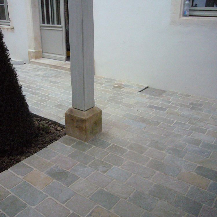Terrasse pavée avec un mur blanc, une porte et un poteau de soutien gris.