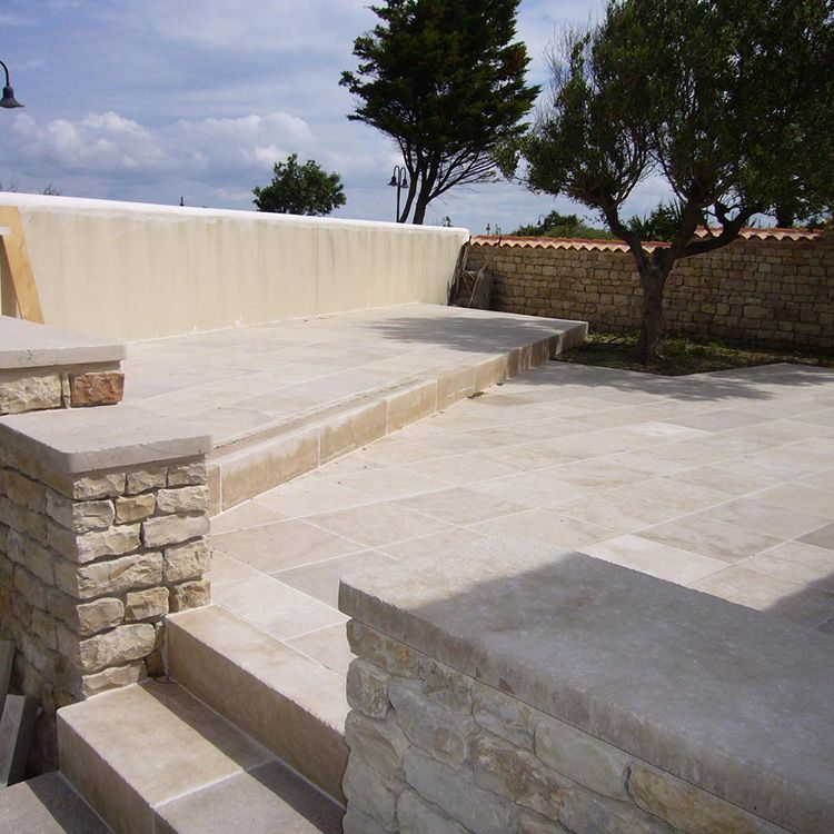 Terrasse en pierre avec marches, banc bas et arbres dans une cour ensoleillée