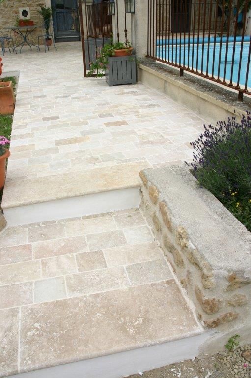 Des marches en pierre mènent à une allée bordant la piscine, agrémentée de jardinières et d'une rambarde en fer forgé.