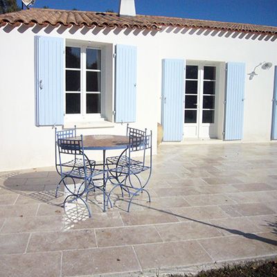 Volets bleus sur un mur de patio blanc avec une table et des chaises en fer forgé devant