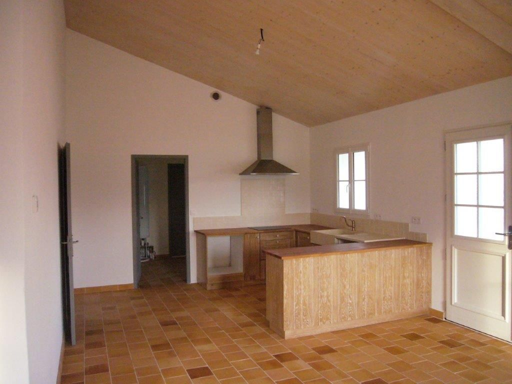 Cuisine vide non meublée avec sol carrelé, plafond en bois, îlot central, hotte aspirante et portes-fenêtres