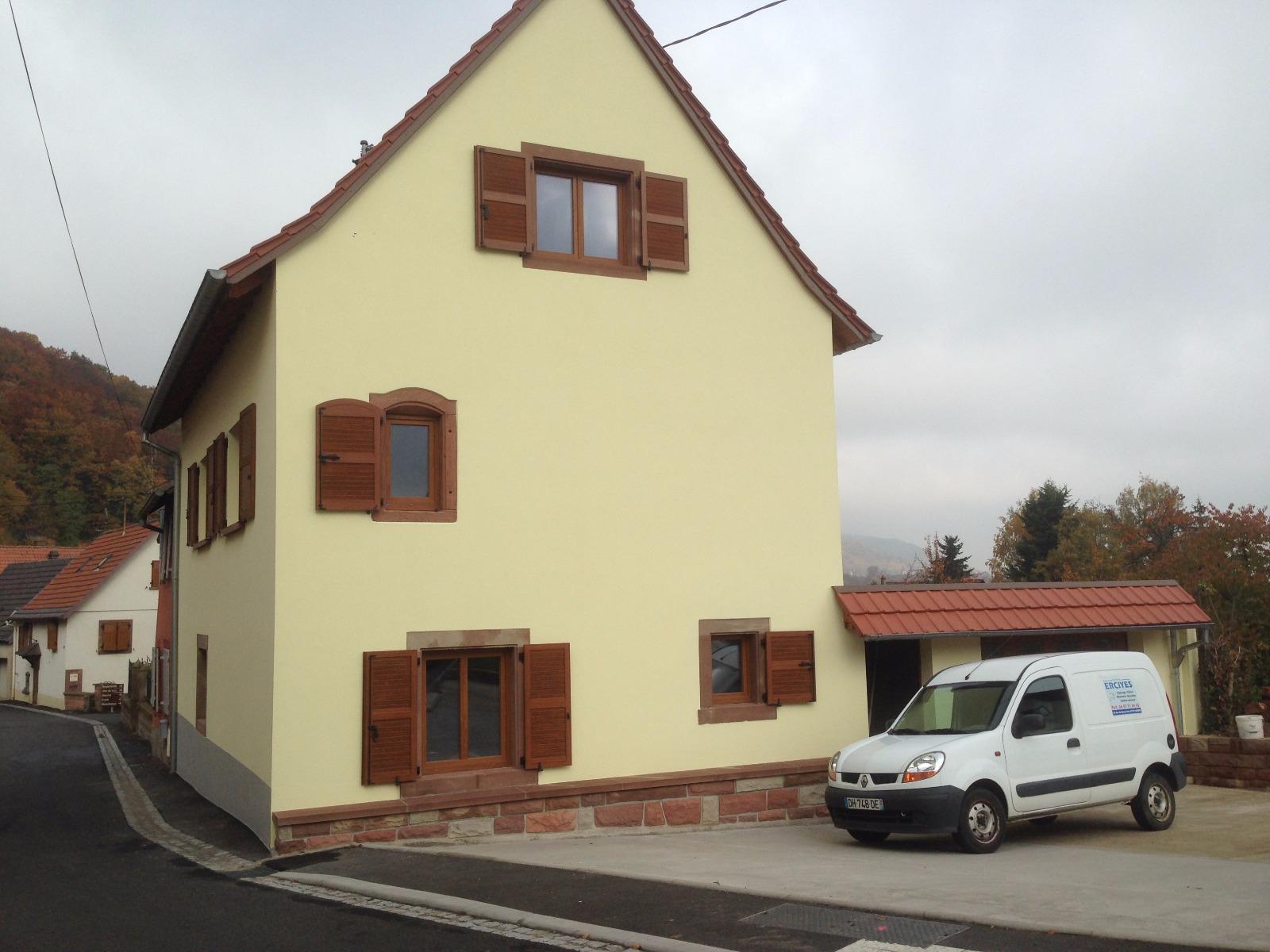 Maison jaune à deux étages avec volets marron. Une camionnette blanche garée à côté.