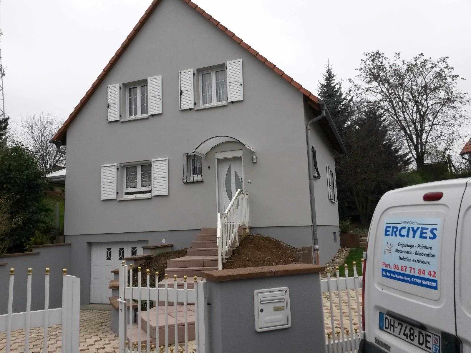 Maison grise avec des volets blancs, un toit rouge et une clôture blanche.