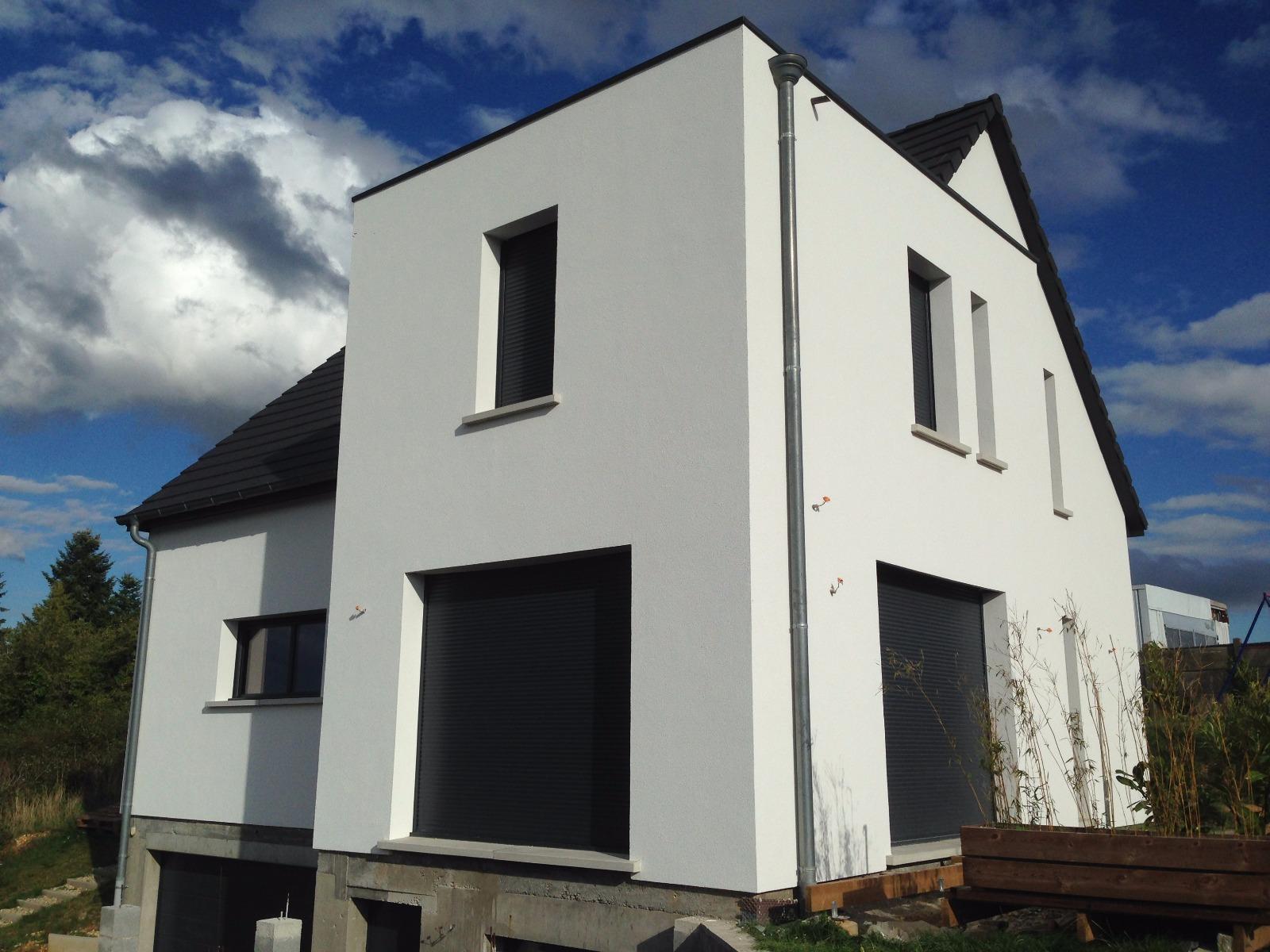 Maison blanche à deux étages avec des volets noirs et un toit sombre.