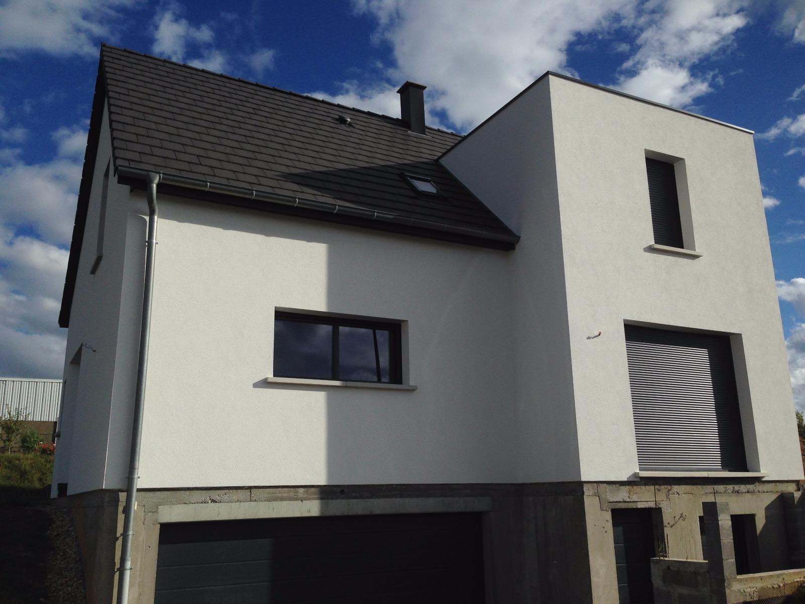 Maison blanche à deux étages avec toit et boiseries foncés, porte de garage grise et store rayé.