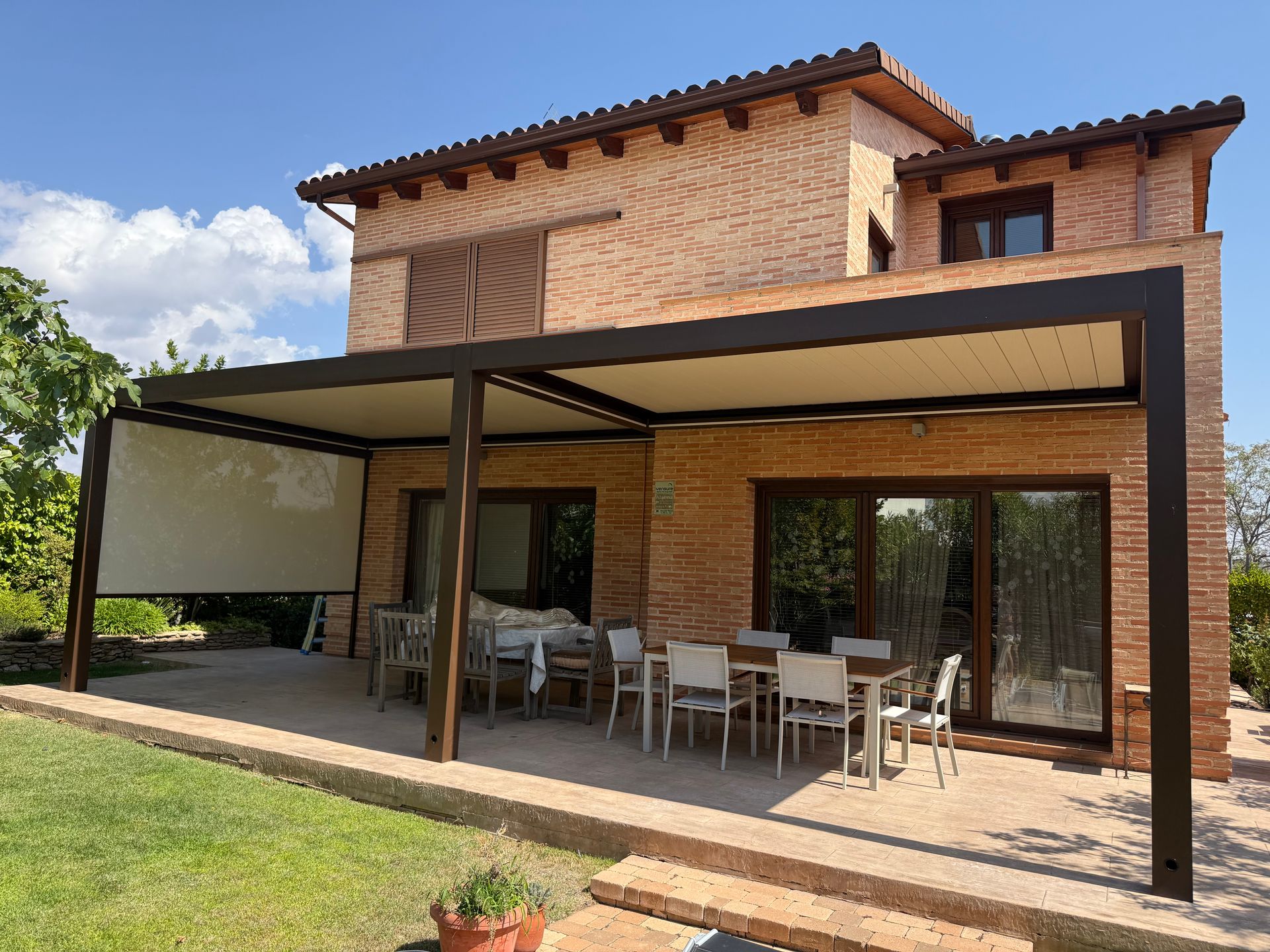 Casa moderna de dos plantas de ladrillo con pérgola de patio con estructura negra y zona de comedor al aire libre.