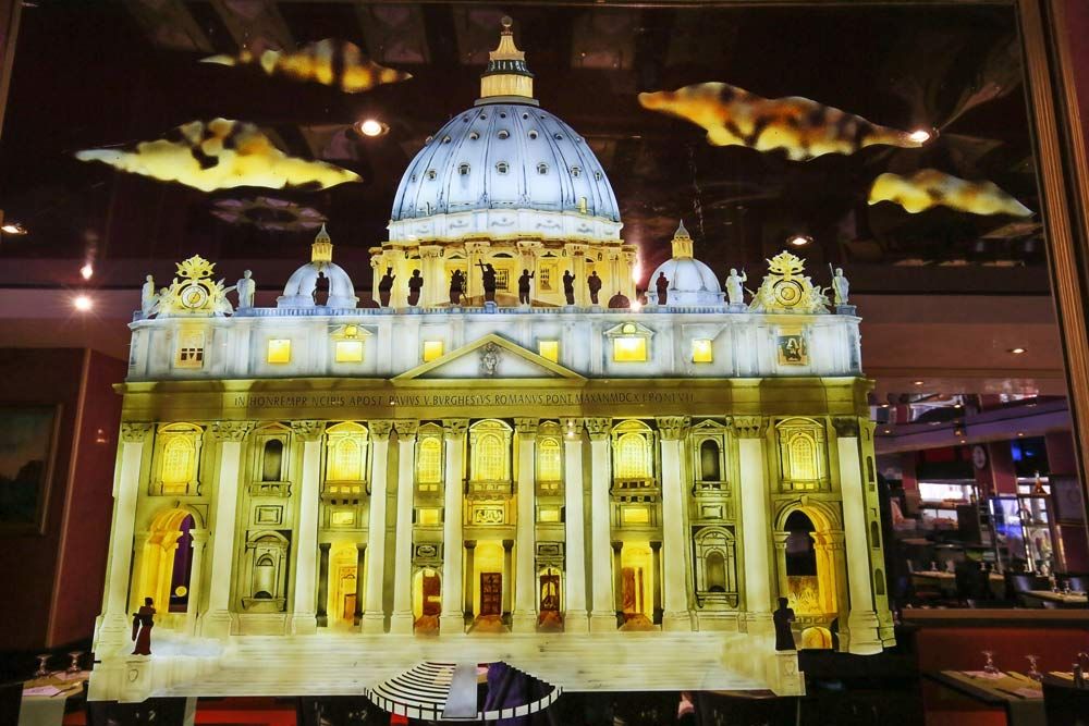 Maquette illuminée de la basilique Saint-Pierre avec son dôme, sur fond sombre intérieur.
