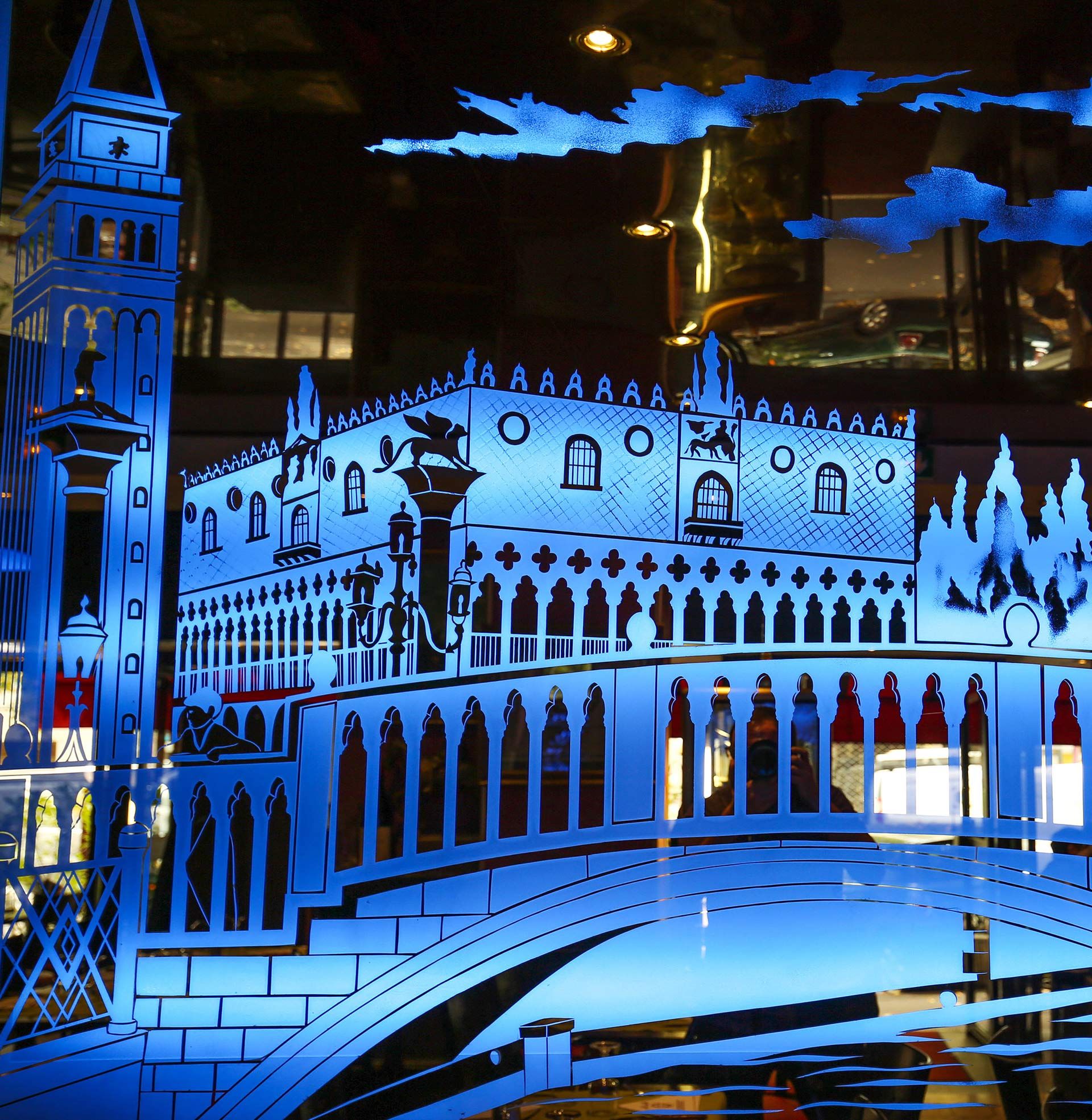 Scène de canal de style vénitien illuminée en bleu, avec un pont orné, un clocher et des bâtiments à arcades la nuit