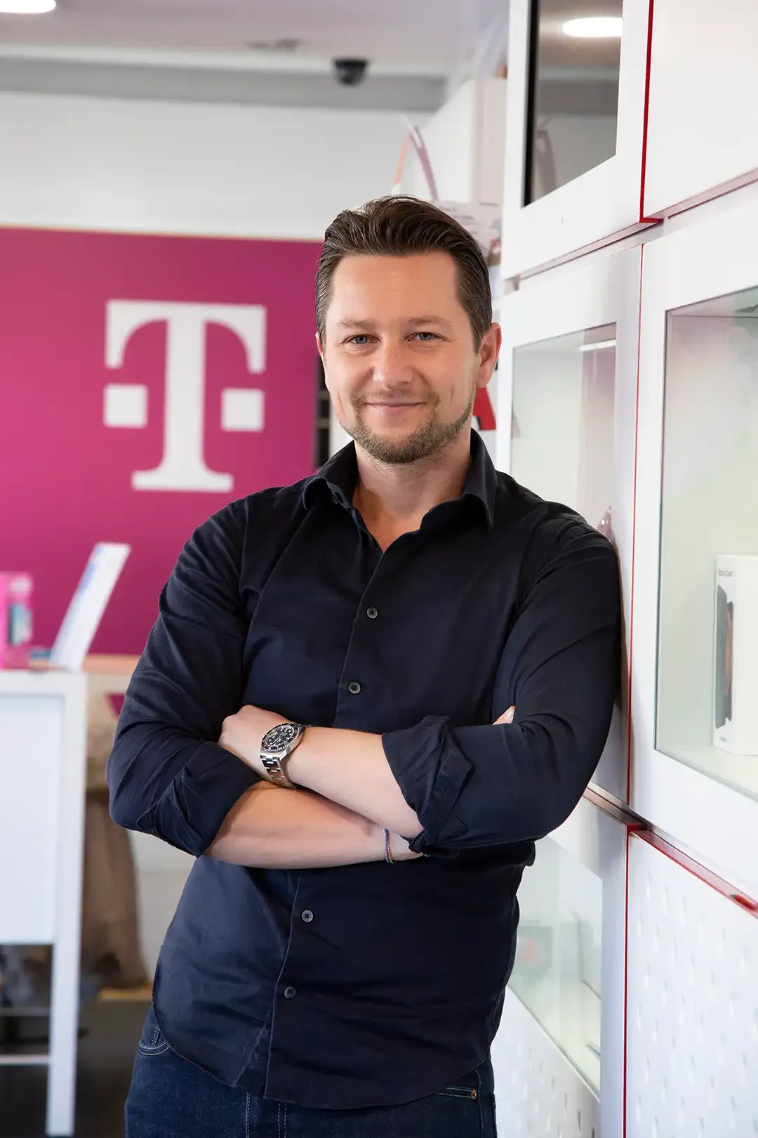 Ein Mann in einem schwarzen Hemd lehnt mit verschränkten Armen an einer Wand.