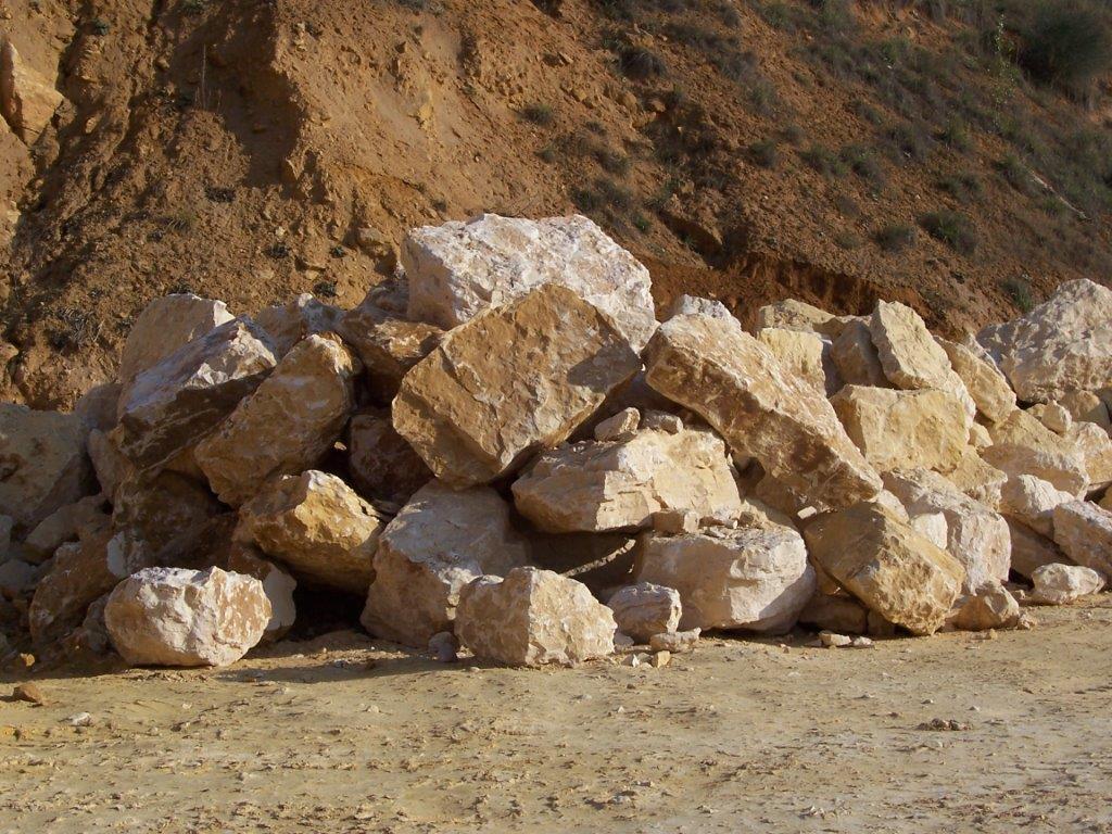 Des tas de pierres pâles et de gravats bordent un chemin de terre au pied d'une colline brune.