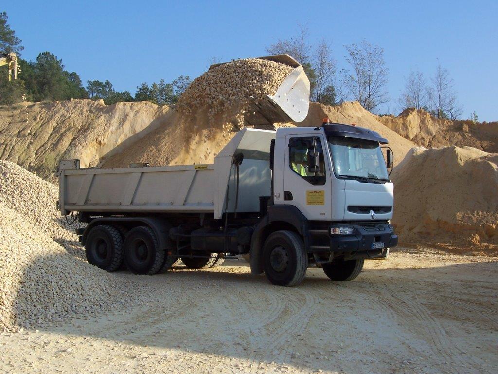 Un camion-benne décharge de la terre sur un chantier de construction, avec des tas de terre en arrière-plan.
