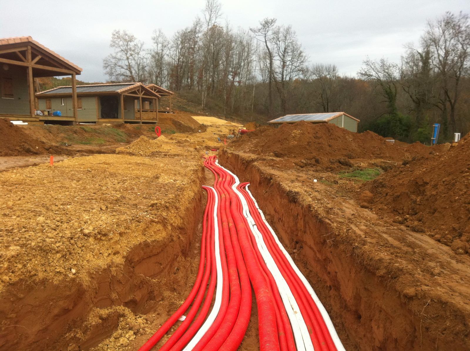 Des tuyaux de service public rouges sont posés dans une tranchée de terre sur un chantier de construction de maison.
