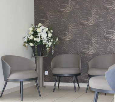 Salle d'attente avec chaises grises, composition florale et mur à motifs.