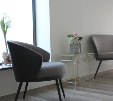 Deux fauteuils gris près d'une fenêtre et une petite table blanche avec des fleurs.