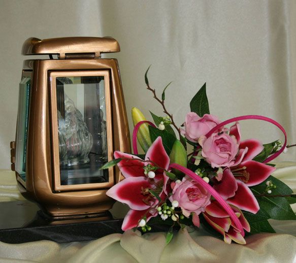 Lanterne en bronze à côté d'un arrangement floral composé de lys et de roses roses.
