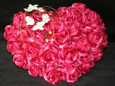 Composition en forme de cœur de roses roses avec des touches d'orchidées blanches sur un fond sombre.