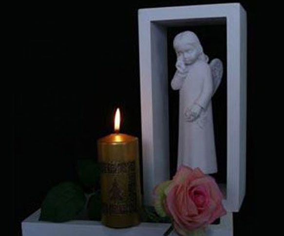 Flamme de bougie à côté d'une statue d'ange, d'une rose rose et d'un fond noir.