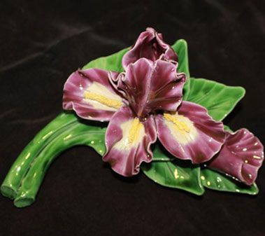 Fleur d'iris violette en céramique à feuilles vertes, sur fond sombre.