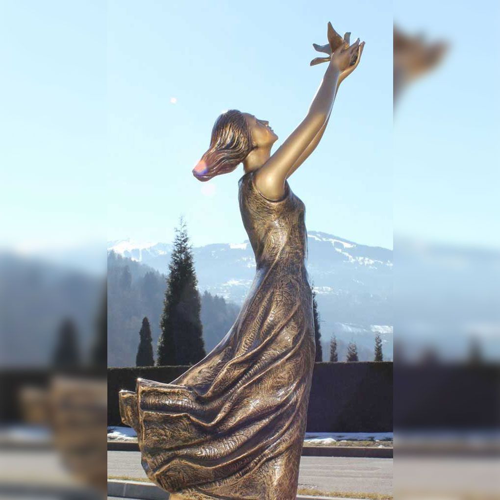 Statue en bronze d'une femme tendant la main vers le ciel, avec des montagnes en arrière-plan.