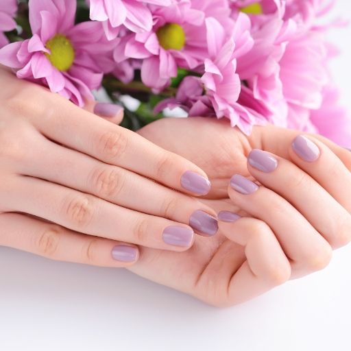 Una mujer con uñas moradas sostiene un ramo de flores rosas.