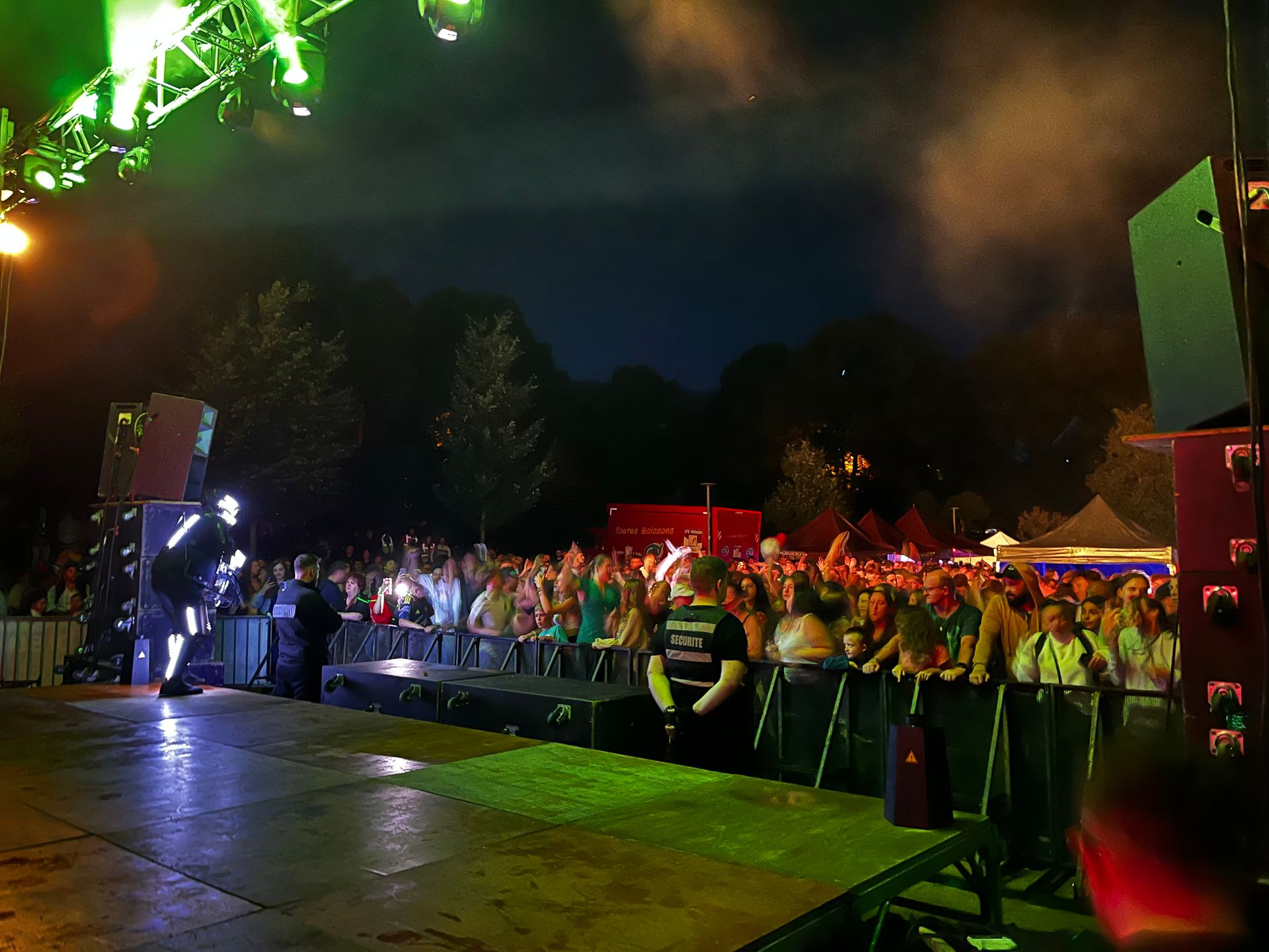Concert nocturne en plein air avec une foule de personnes regardant un groupe sur scène, éclairage vert.