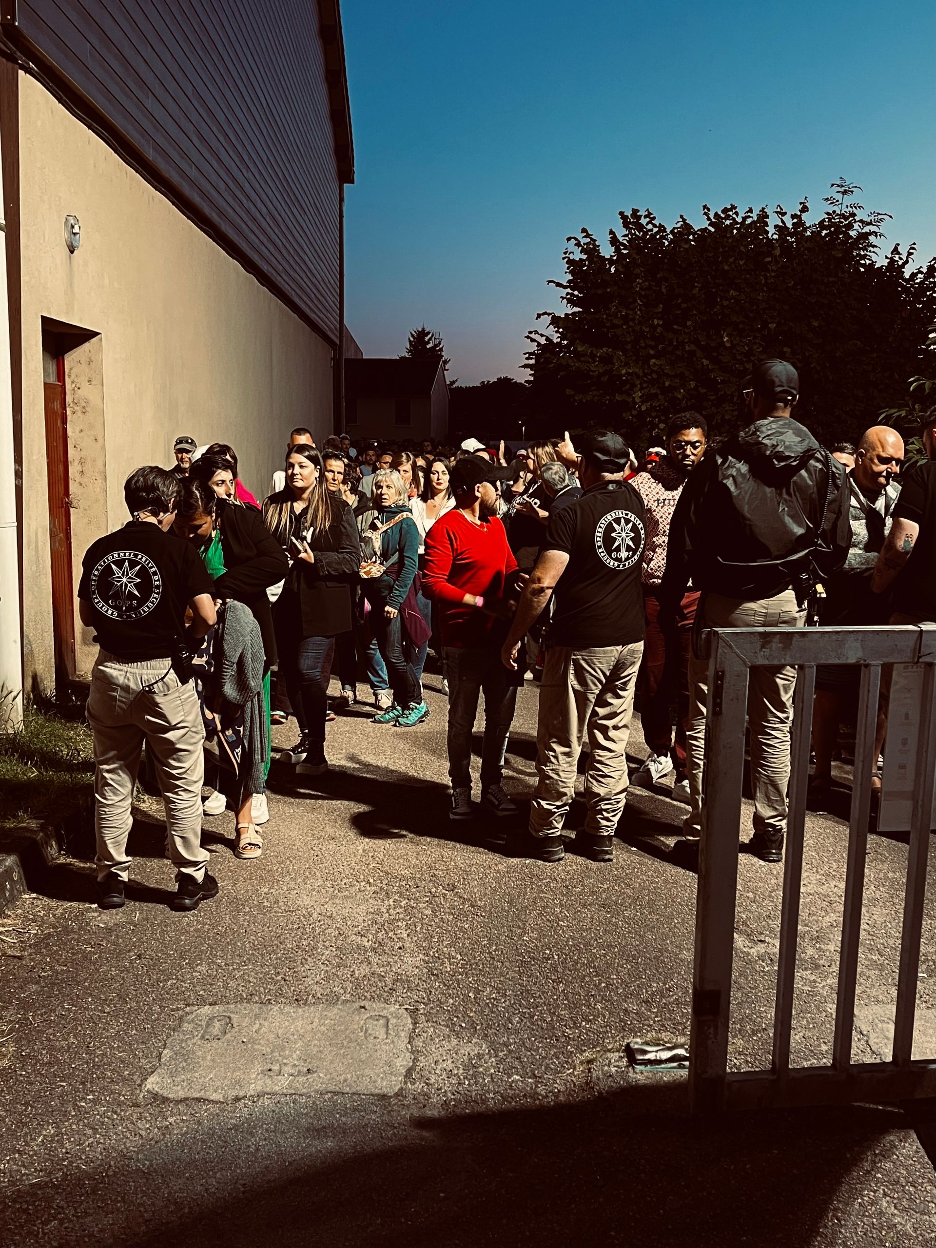 Des gens se sont rassemblés près d'un bâtiment, certains portant des chemises noires assorties avec un logo. En journée.