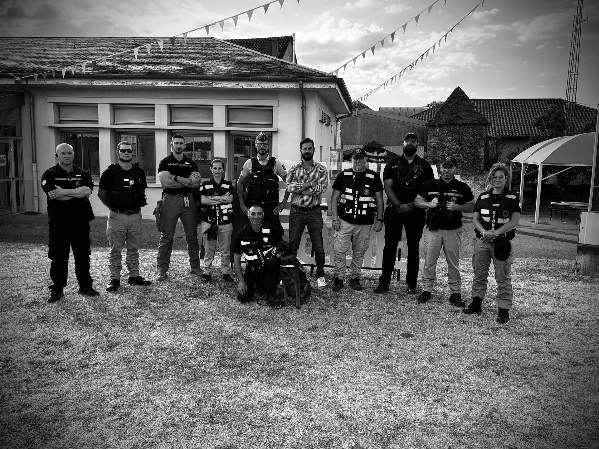 Groupe de personnes en uniforme devant un bâtiment. Plusieurs portent des gilets. Photo en noir et blanc.