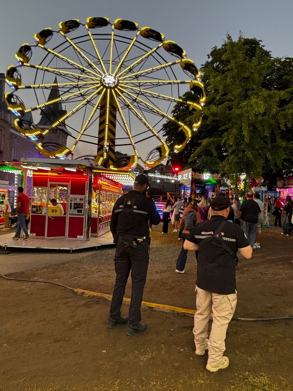 Deux agents de sécurité lors d'un carnaval brillamment éclairé, avec une grande roue en arrière-plan.