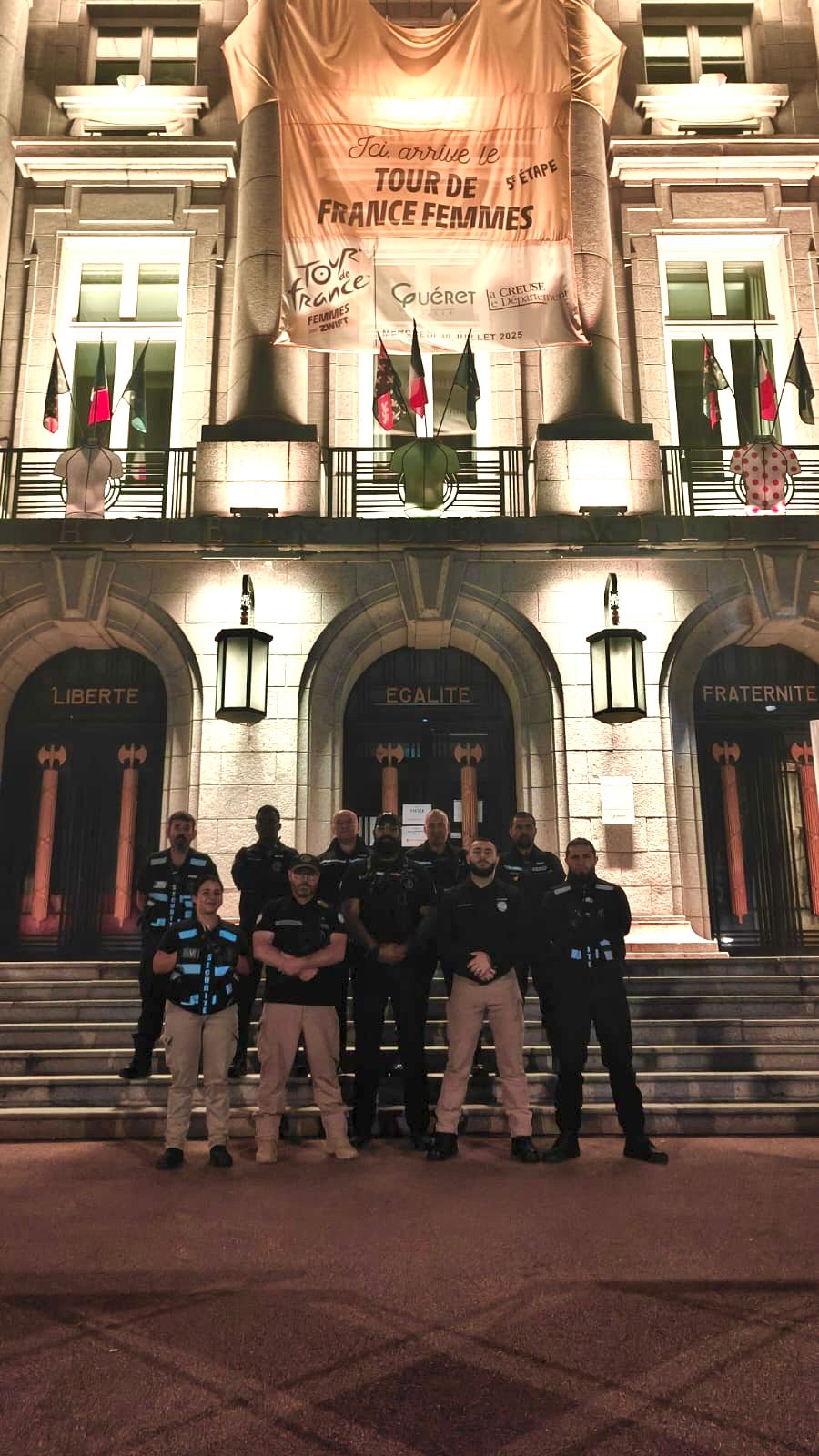 Un groupe d'hommes en uniforme pose devant un bâtiment illuminé la nuit. Bannière en haut.