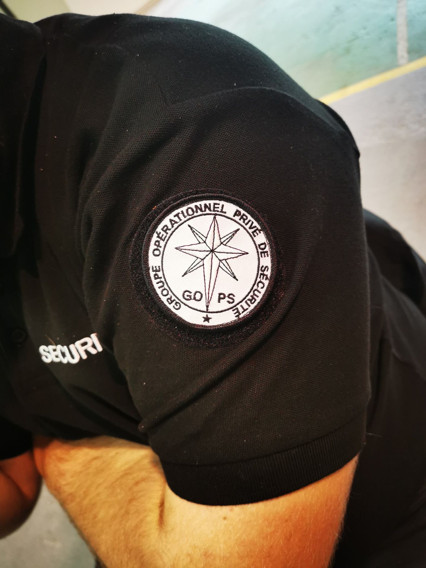 Gros plan sur une manche d'uniforme noire ornée d'un écusson circulaire. L'écusson arbore une rose des vents et l'inscription « GROUPE OPERATIONNEL PRISE DE SÉCURITÉ ».