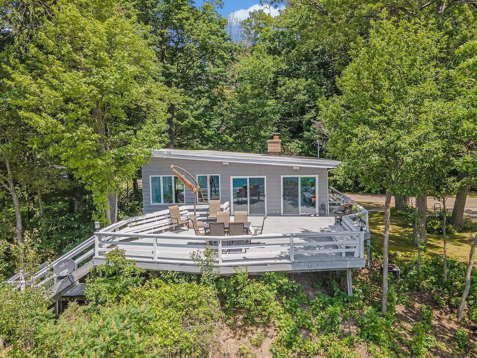 Lakefront house with a large deck surrounded by trees.