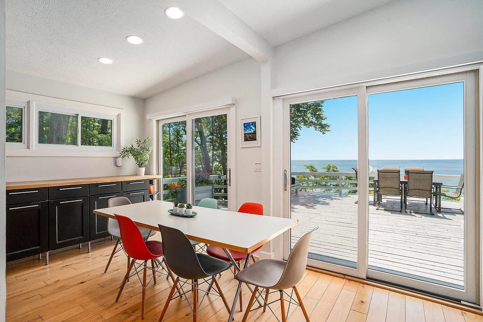 Dining room with table, chairs, cabinets, and large windows overlooking a deck and water.