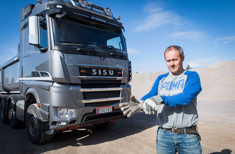 Mies pukee hanskojaan hopeanvärisen SISU-kuorma-auton vieressä sorakuopalla.