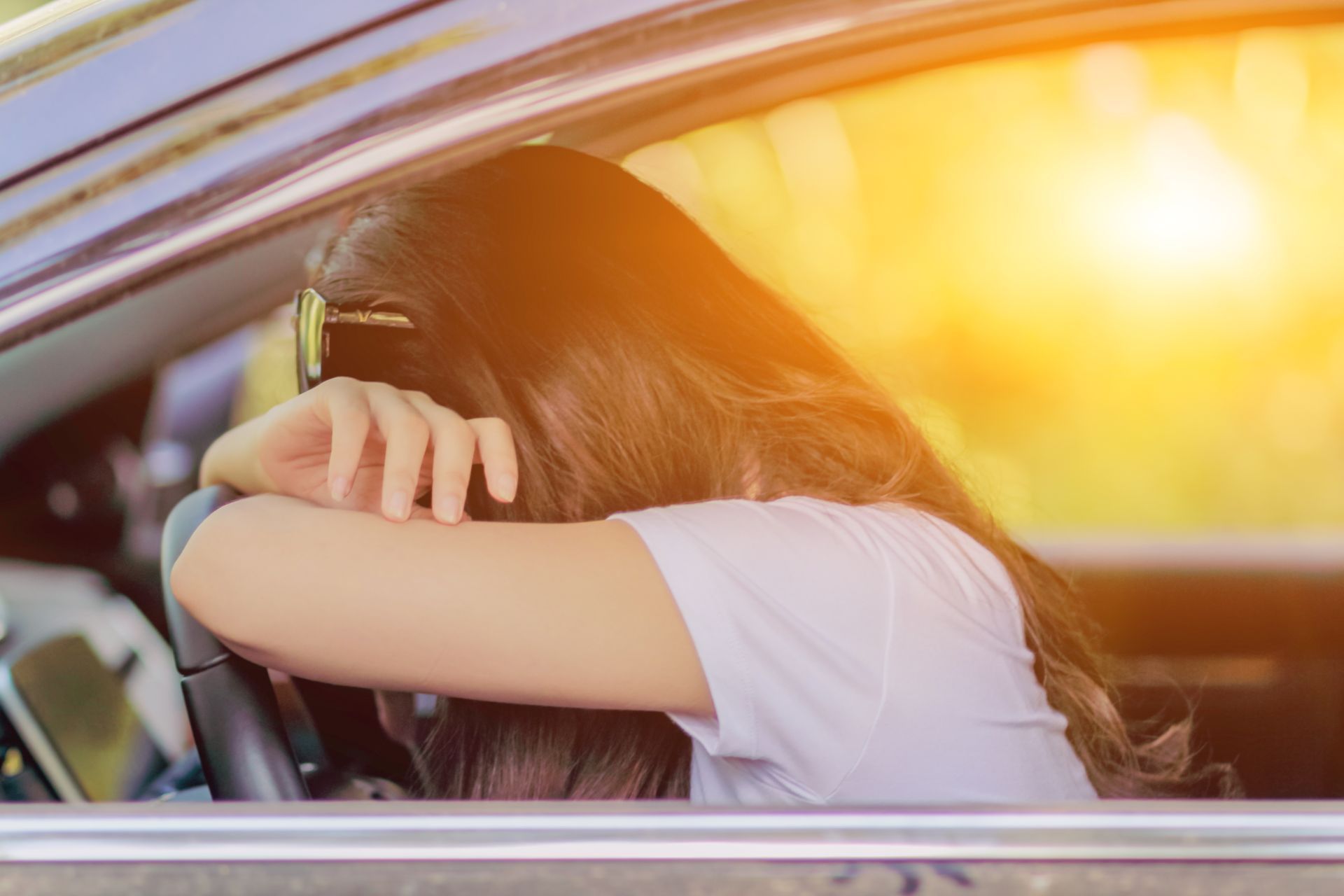 Eine Frau sitzt in einem Auto und lehnt mit den Armen und Kopf auf dem Lenkrad.