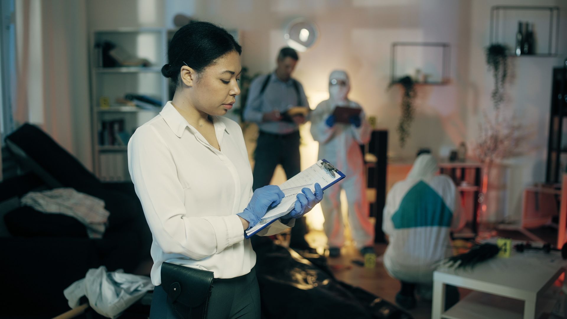 Eine Polizistin mit Team leiten ein Ermittlungsverfahren und untersuchen eine Wohnung.