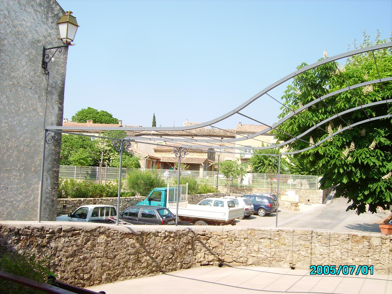 Un parking avec plusieurs voitures. Un mur de pierre se trouve au premier plan et des bâtiments à l'arrière-plan.