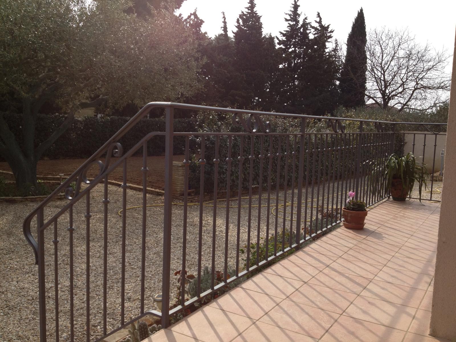 Rambarde métallique sur une terrasse donnant sur un jardin arboré, par une journée ensoleillée.