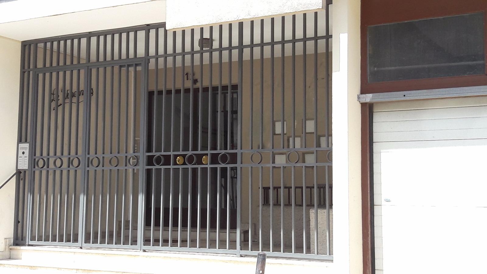 Portail métallique noir devant l'entrée d'un immeuble. Porte et boîtes aux lettres visibles.