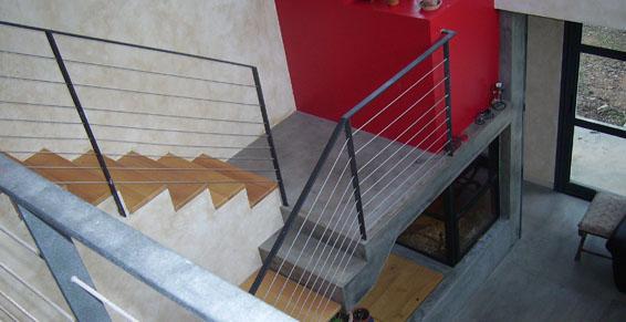 Escalier avec marches en bois et rampe en métal. Mur rouge en arrière-plan. Lumière naturelle provenant d'une fenêtre.