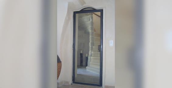 Un miroir en pied, encadré de noir, est fixé sur un mur clair. Un escalier s'y reflète.